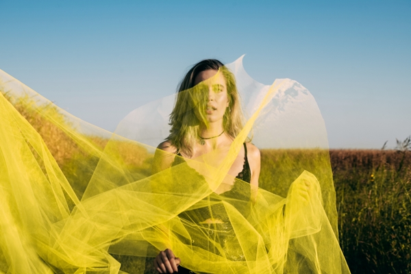 Tendencias primavera verano 2024 - Mujer usando un top color negro detrás de una tela de transparencia amarilla en un campo