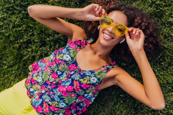 Tendencias primavera verano 2024 - Mujer usando una blusa de estampados de flores acostada sobre el pasto
