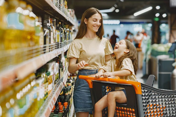 Supermercados en Madrid - Mujer joven sonriendo mientras lleva a una niña sentada en el coche de compras del supermercado en Madrid