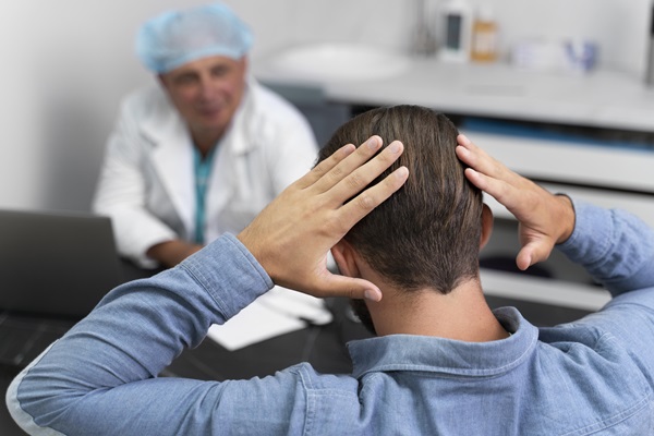 Mejores clínicas de injerto capilar Barcelona - Hombre tocándose la cabeza mientras conversa con un médico especialista en trasplante capilar Barcelona