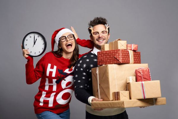Pareja con regalos y ropa navideña cuenta las horas para Nochebuena