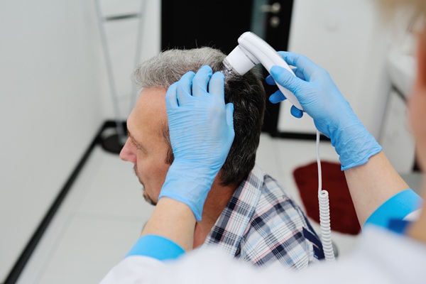 Ventajas del injerto capilar Turquía - Médico tricólogo evaluando el cuero cabelludo de un hombre con instrumentos de tecnología avanzada