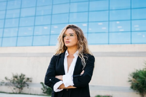 mujer rubia, con traje ejecutivo parada frente a una empresa